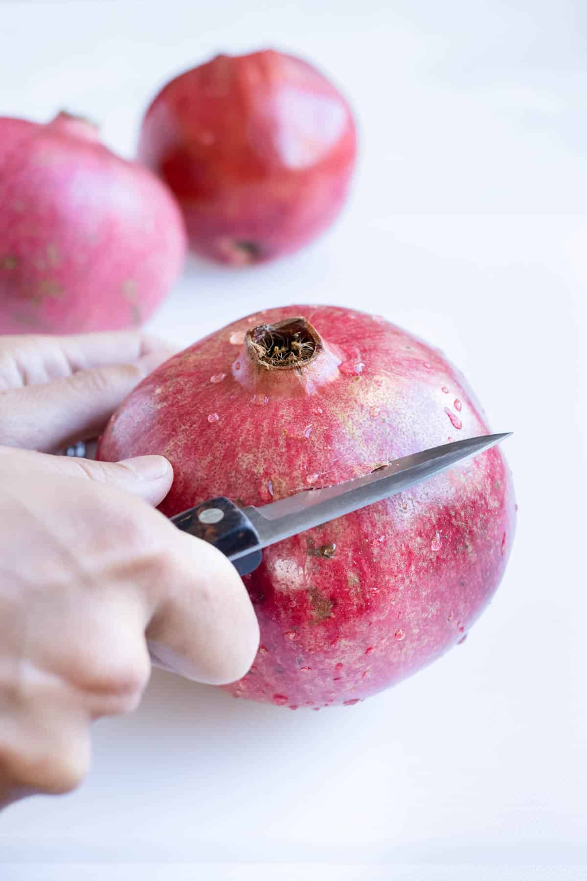 A knife is used to cut the top off of a pomegranate.