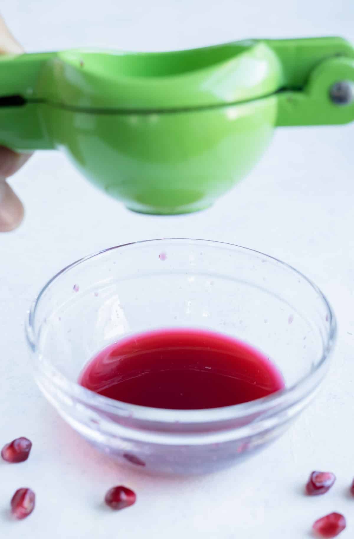 Pomegranate seeds are juiced into a bowl.