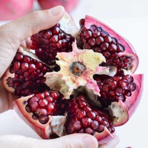 Sections of a pomegranate are separated from the center with two hands.