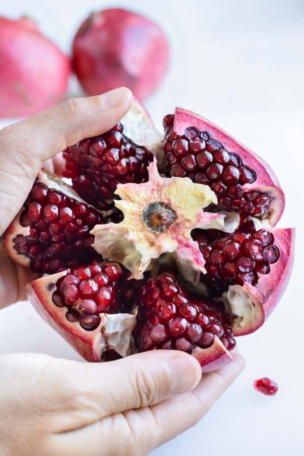 Sections of a pomegranate are separated from the center with two hands.