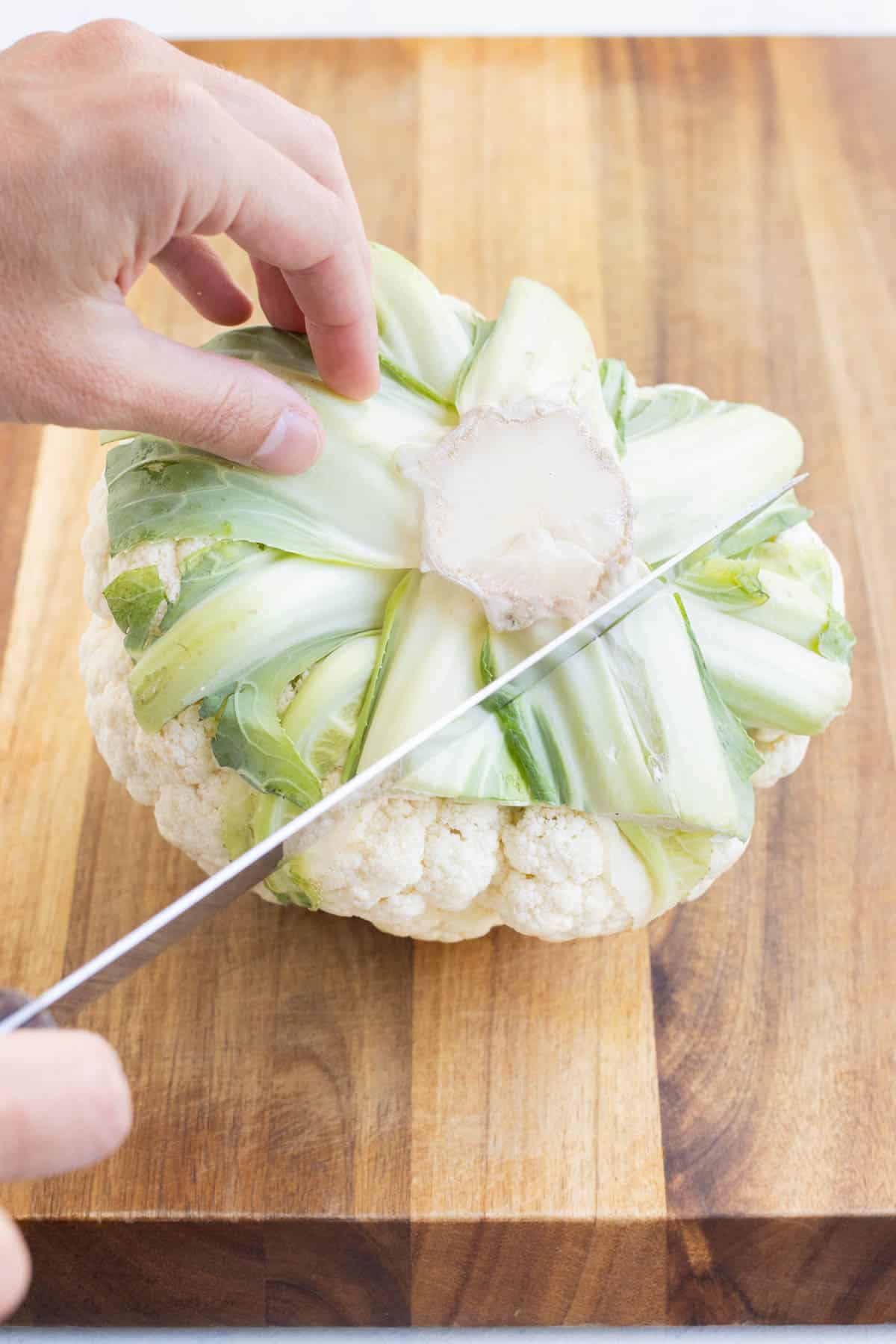 A knife slices away the leaves from a head of cauliflower.