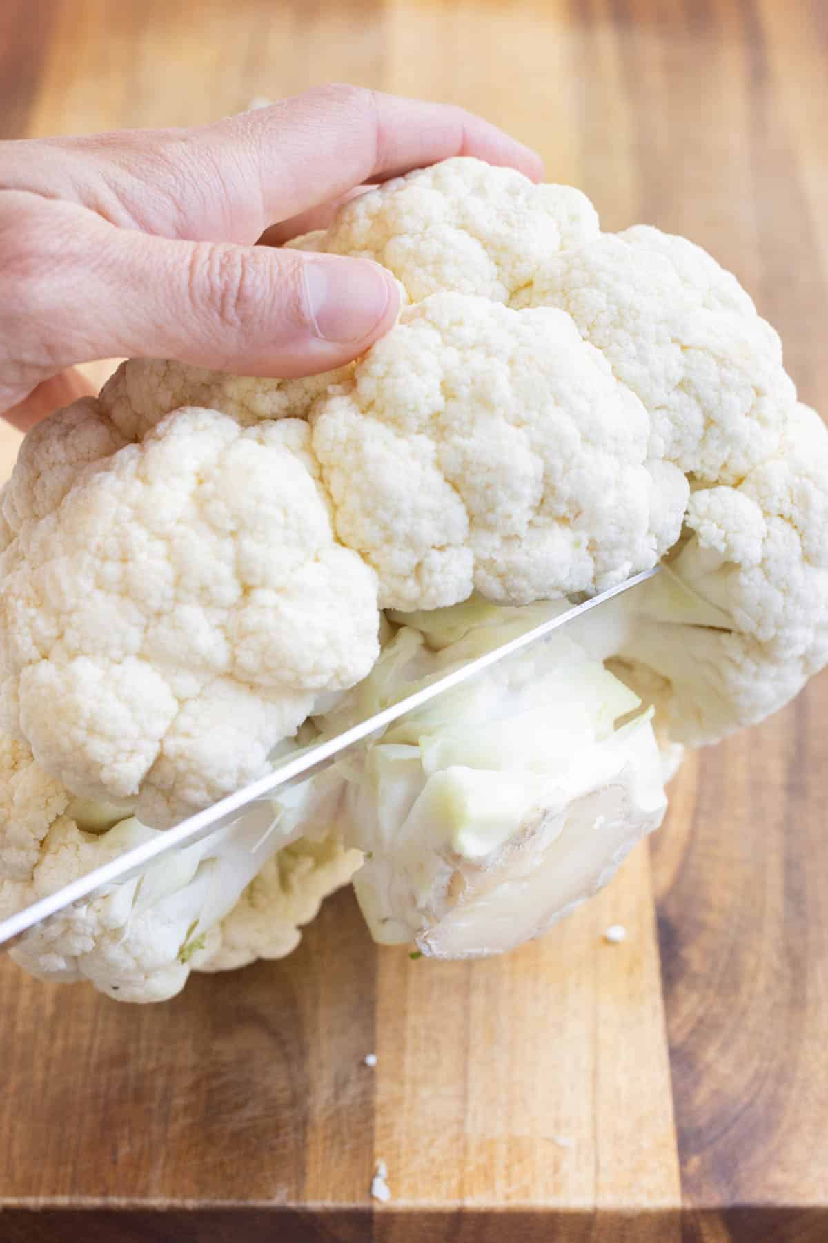 A knife cuts away the bulky stalk from the cauliflower.