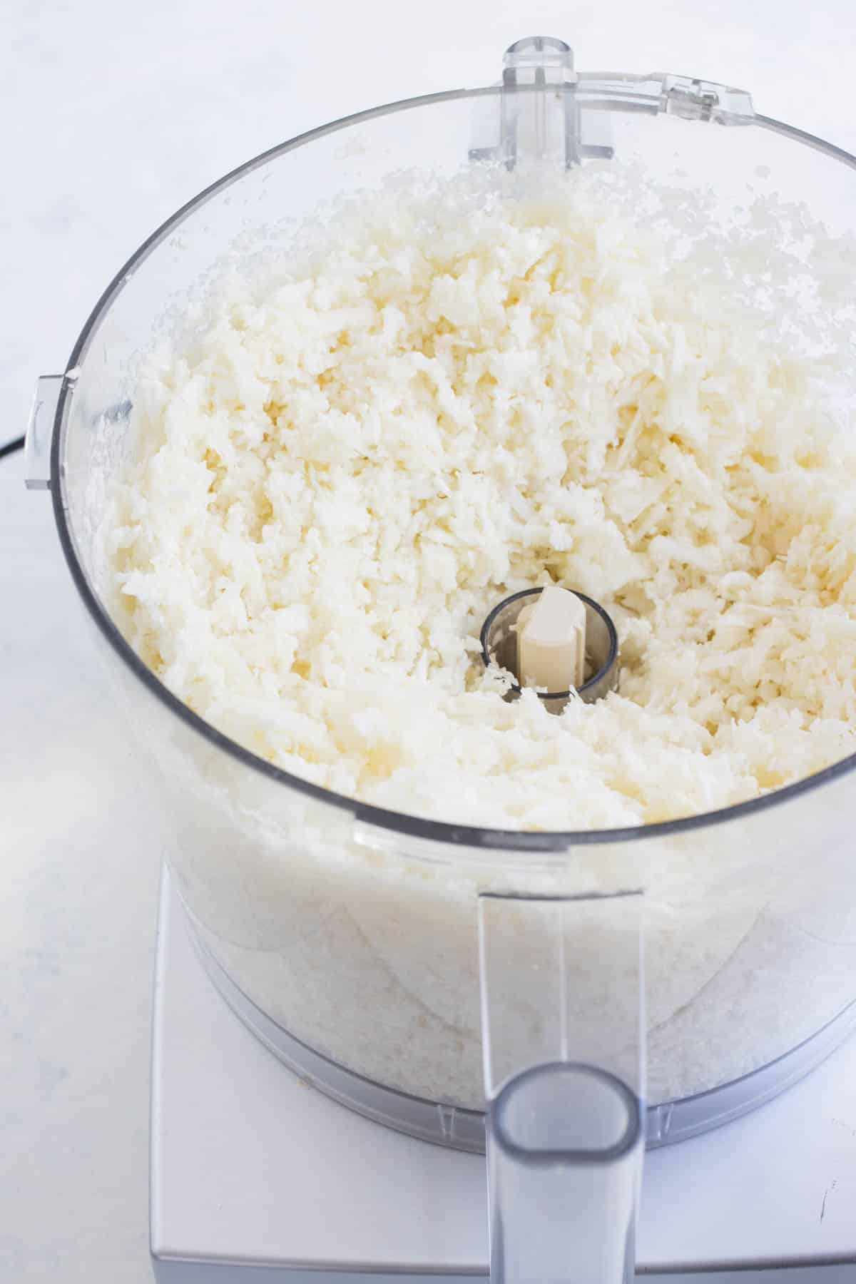 A food processor is full of grated cauliflower.