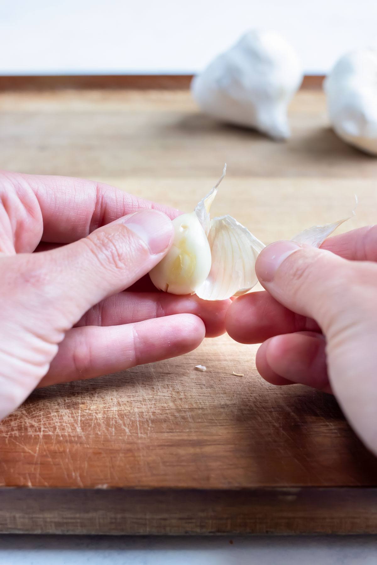 The skin is peeled from a garlic glove using your hands.