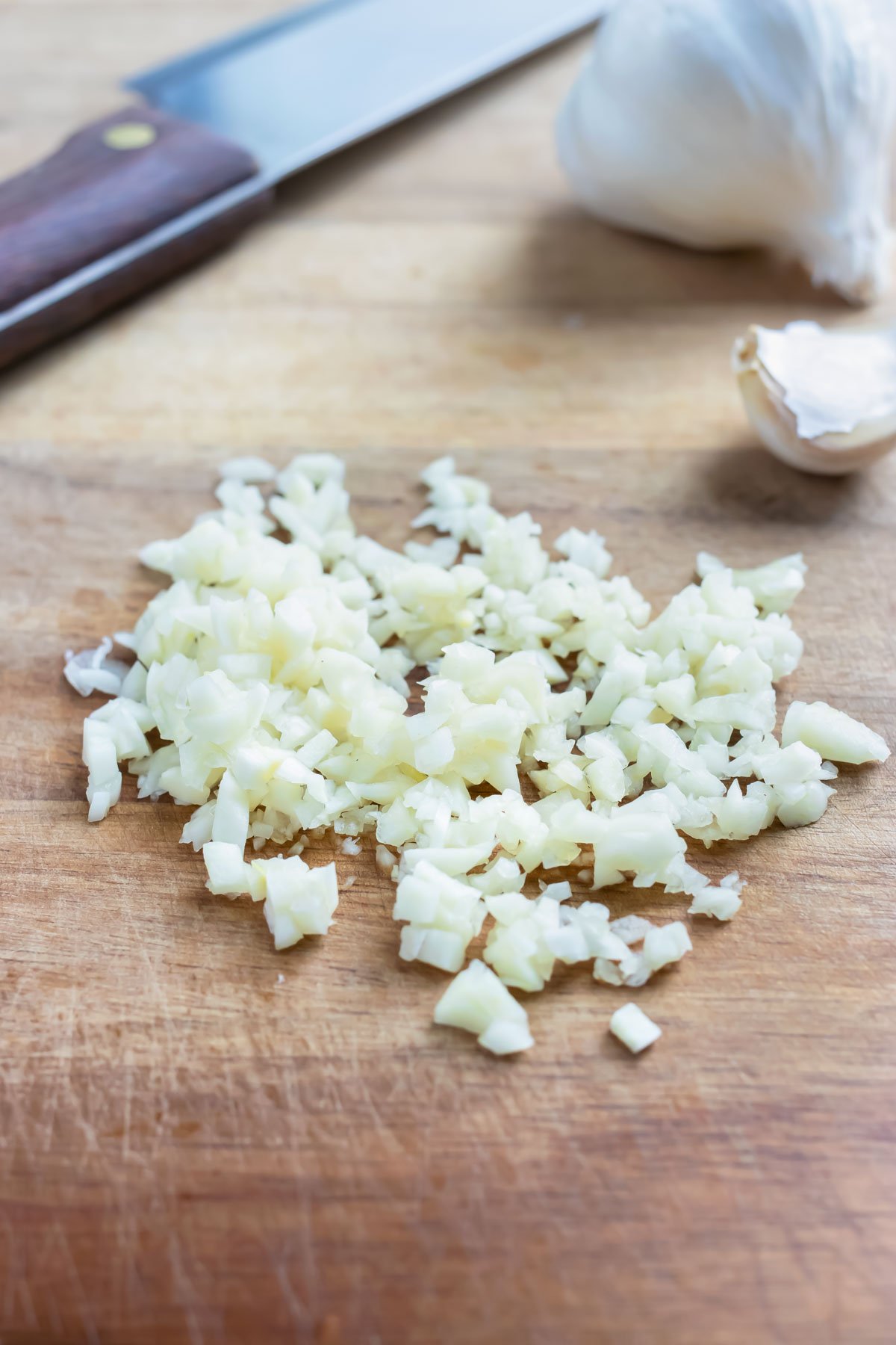 Minced garlic is shown on a cutting board next to a knife.