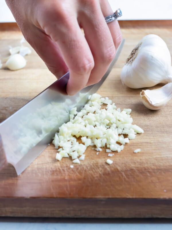 A knife is used to finely chop the garlic on cutting board.