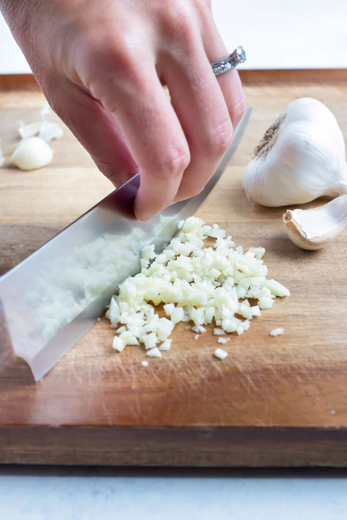 A knife is used to finely chop the garlic on cutting board.