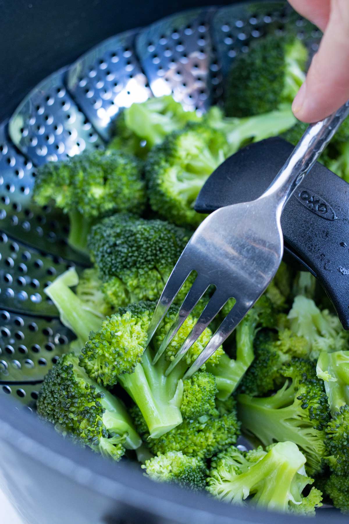 A fork checks for doneness in steamed broccoli.