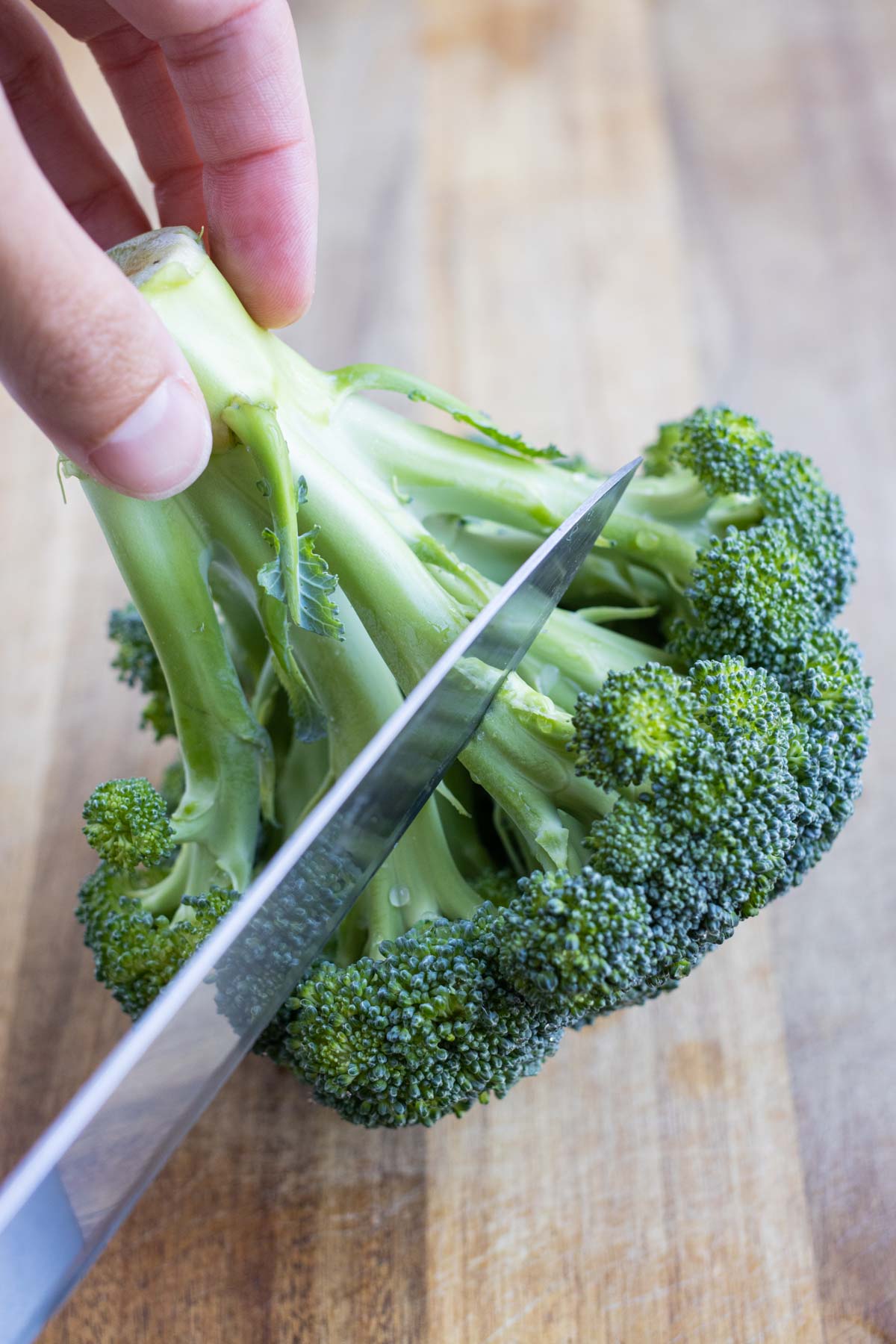 A knife removes the crown of the broccoli from the stem.