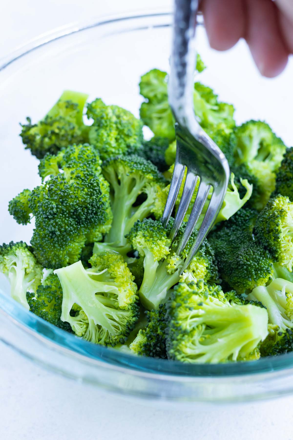 A fork pierces a piece of steamed broccoli.