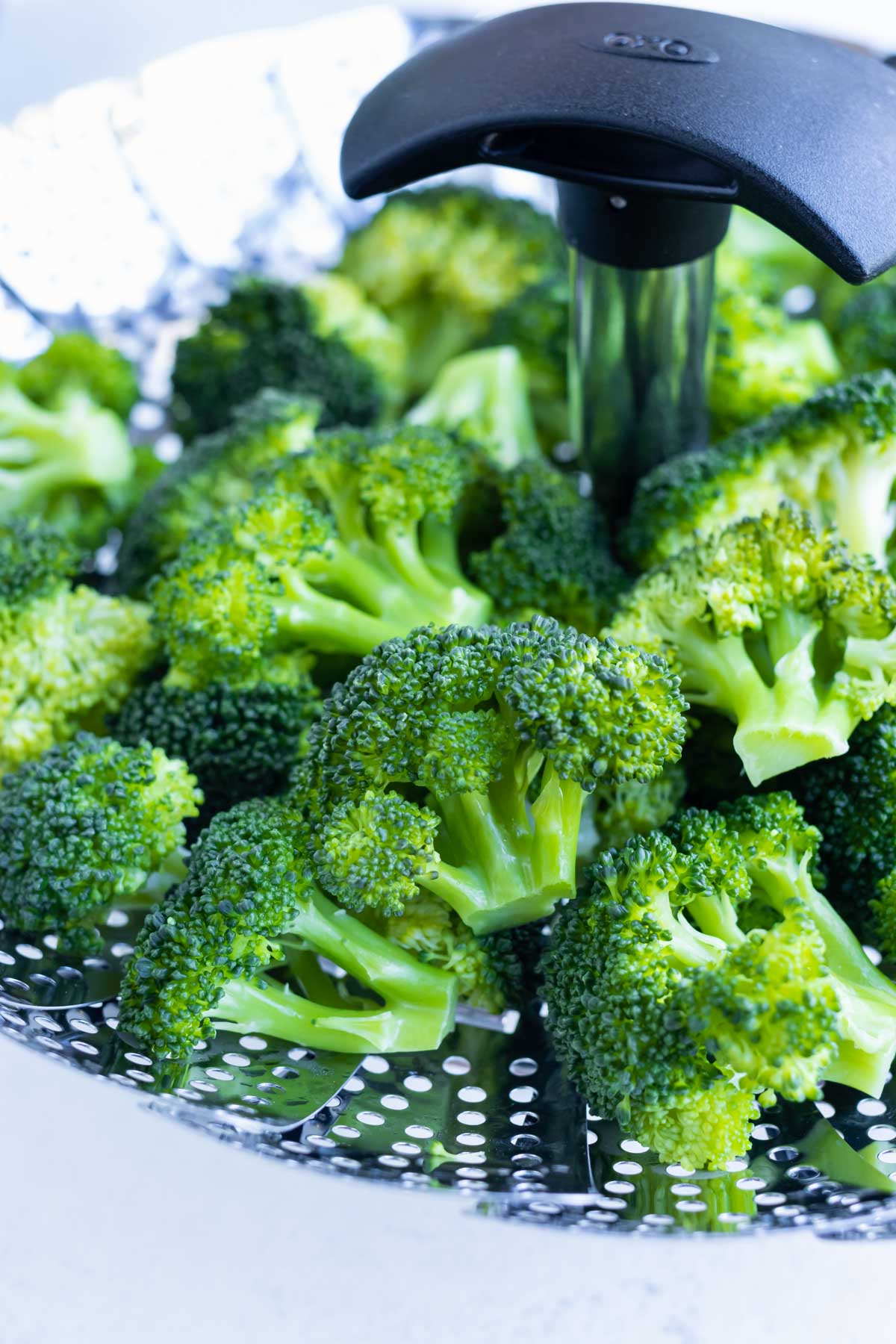 A closeup of steamed broccoli in a steamer basket.