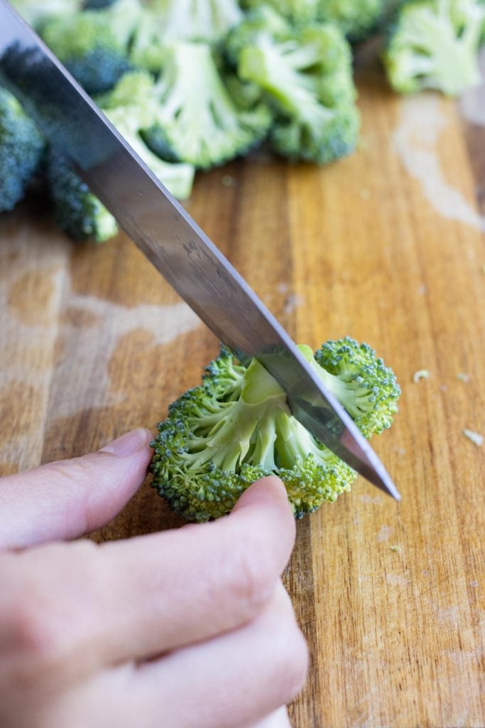 A knife cuts the broccoli florets into bite-sized pieces.