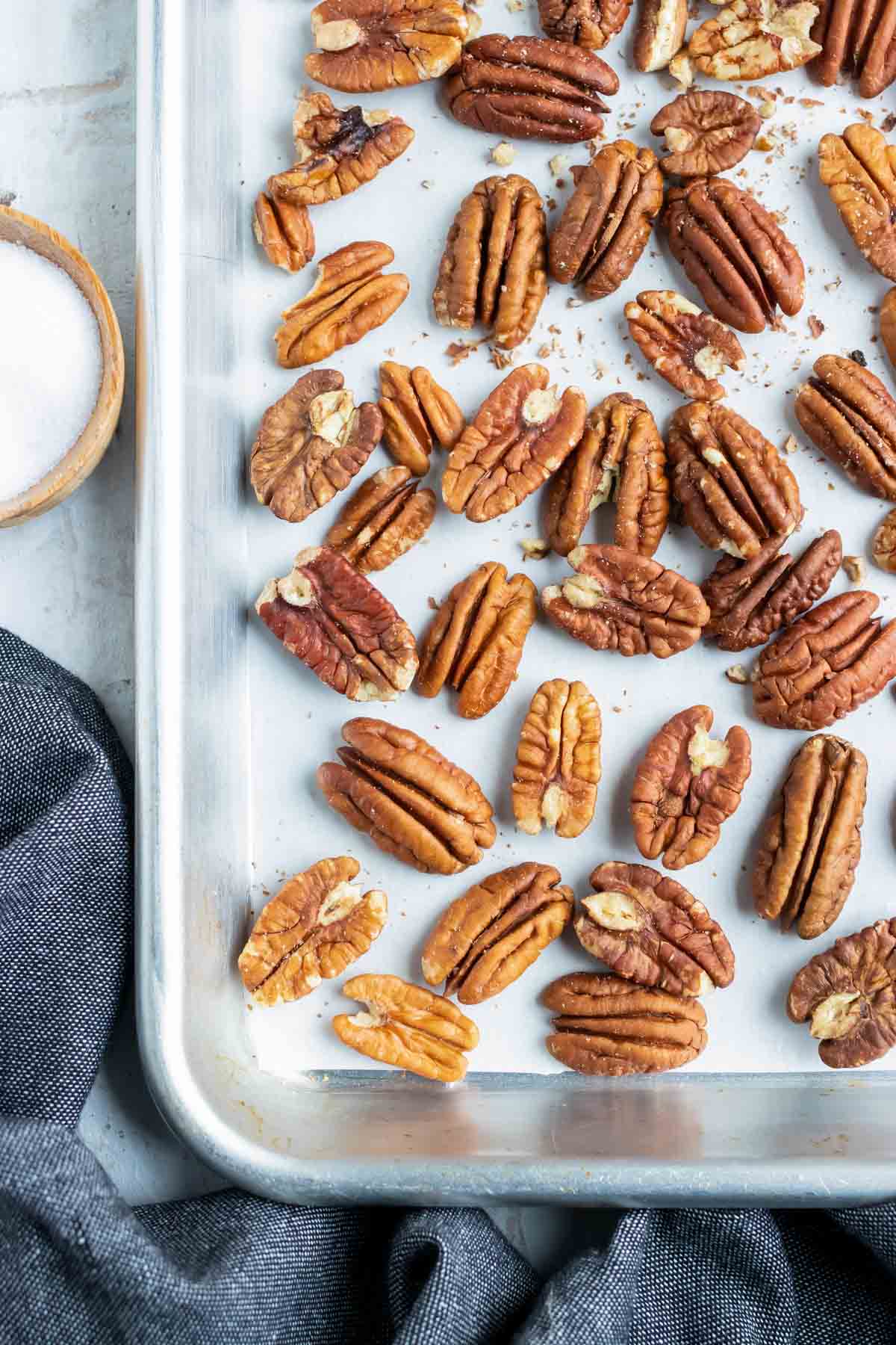 A baking sheet with a layer of pecans showing how to toast pecans in the oven.