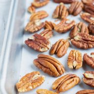 Toasted pecans on a large baking sheet that are going to be roasted in the oven.