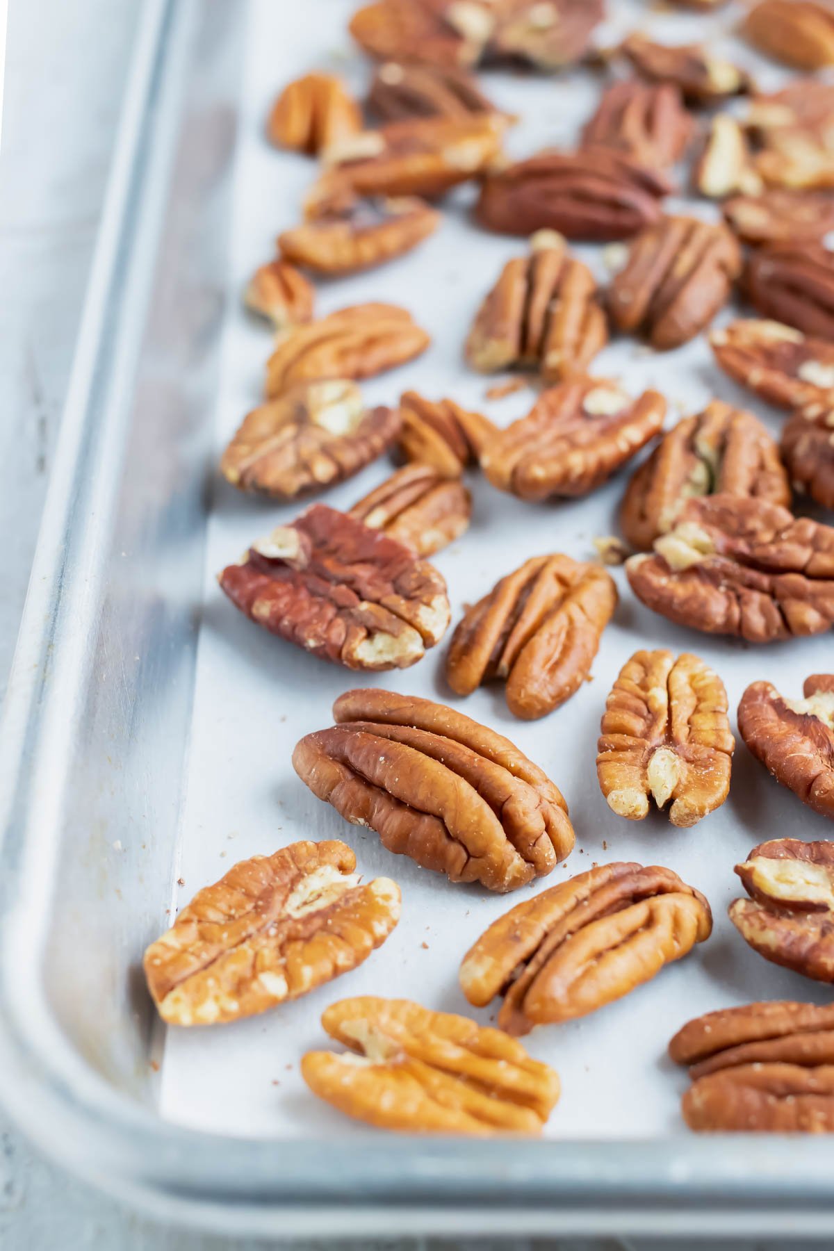 Toasted pecans on a large baking sheet that are going to be roasted in the oven.