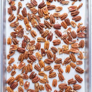 A baking sheet with a layer of pecans showing how to roast pecans in the oven.