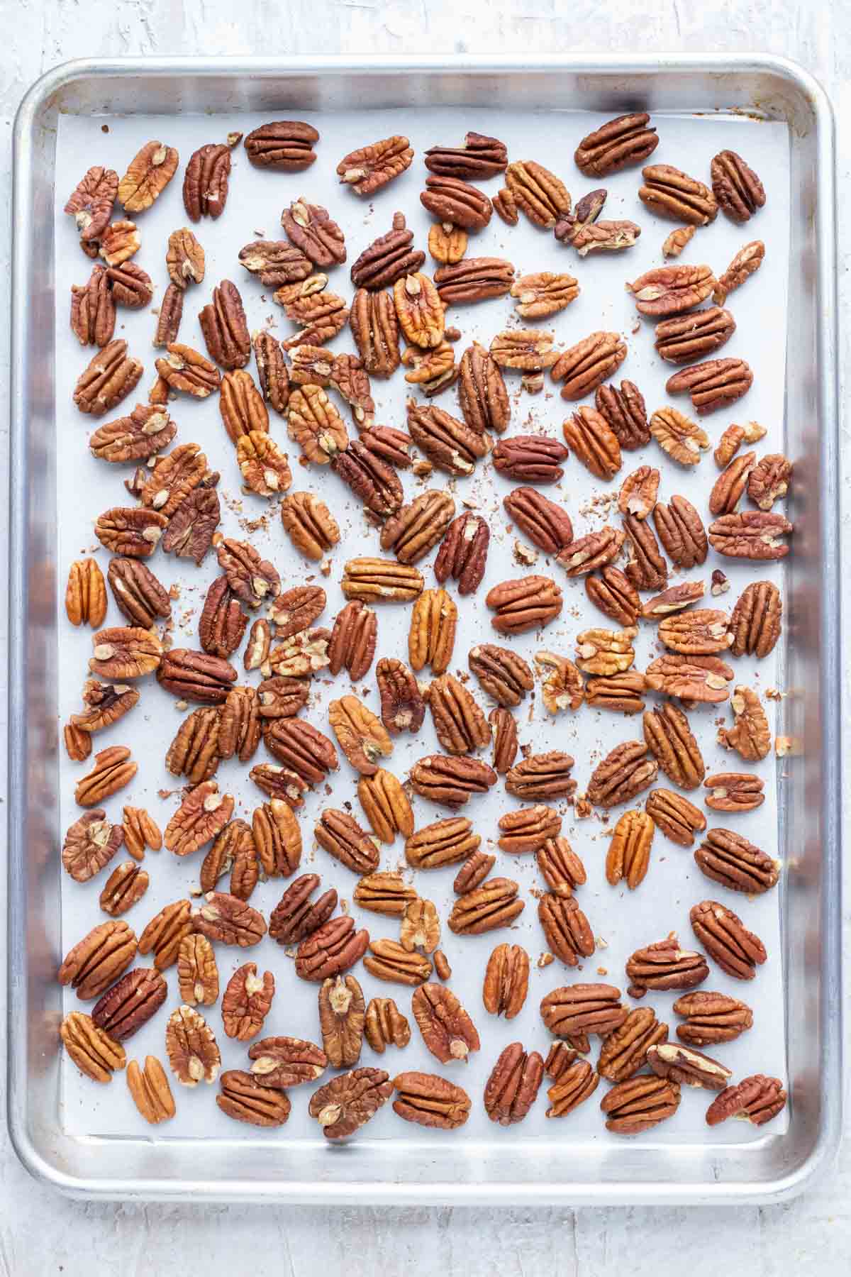 A baking sheet with a layer of pecans showing how to roast pecans in the oven.