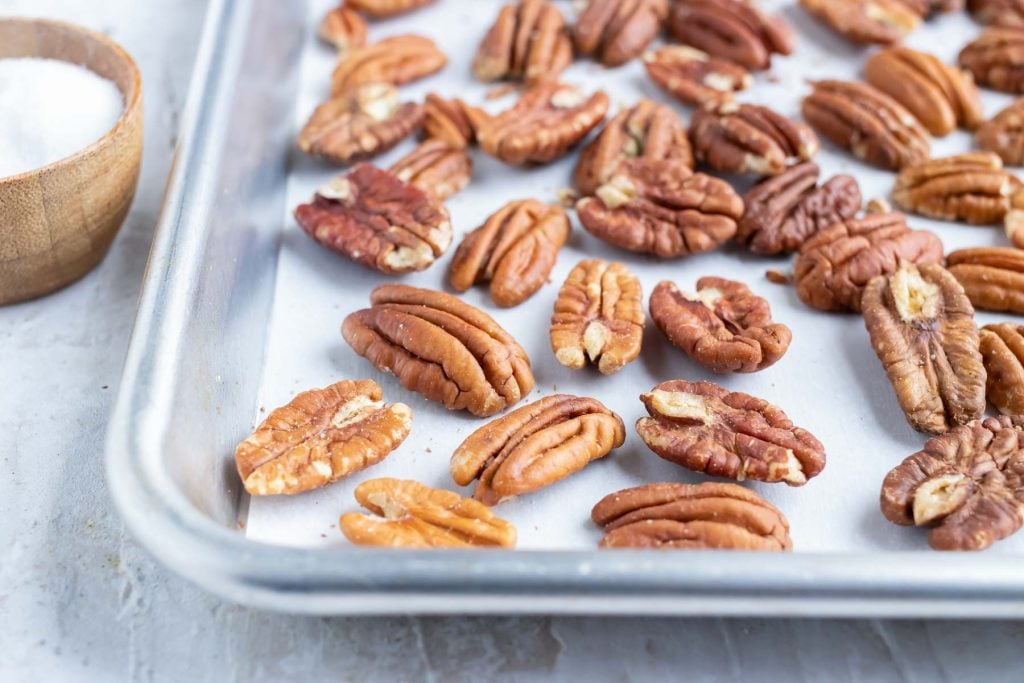 Pecans are placed in a single layer on a baking sheet to be roasted in the oven.