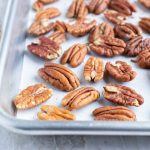 Toasted pecans on a baking sheet with parchment paper.