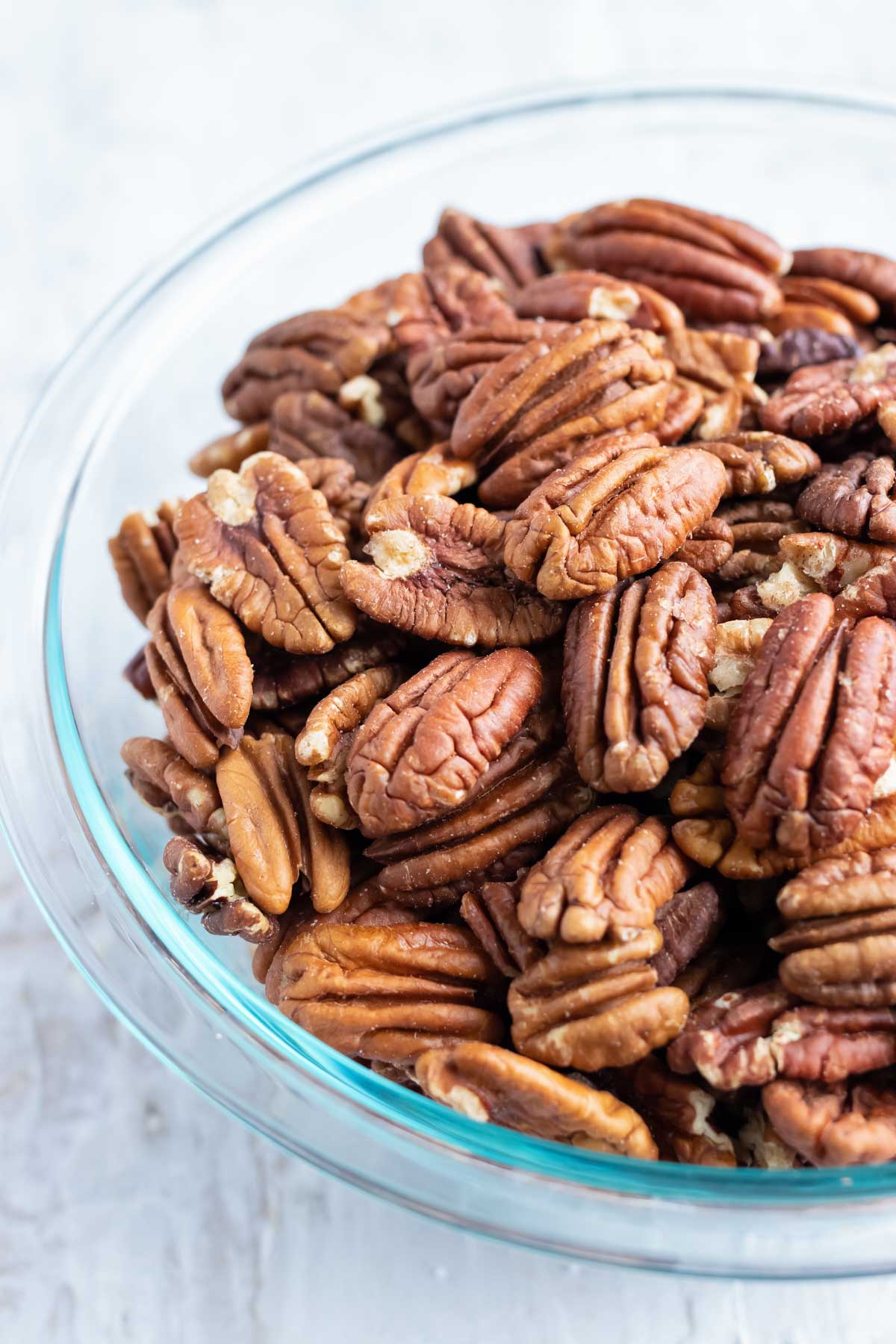 A clear bowl full of raw pecans before they are toasted in the oven.