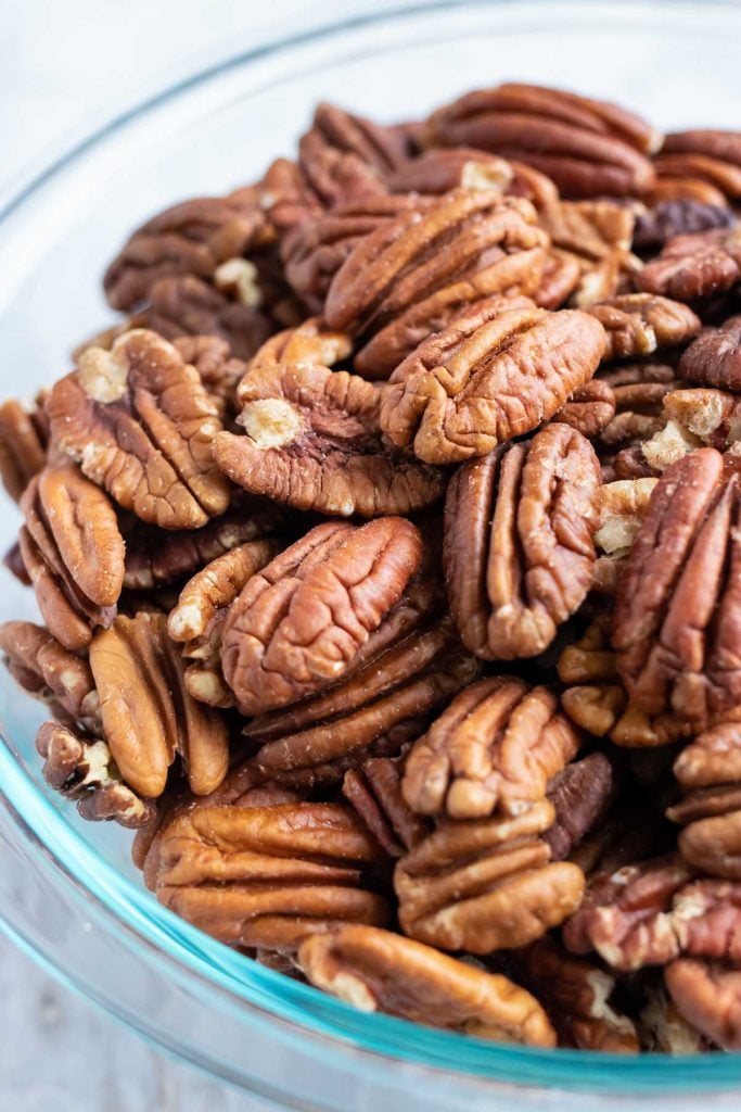 A clear bowl full of raw pecans before they are toasted in the oven.