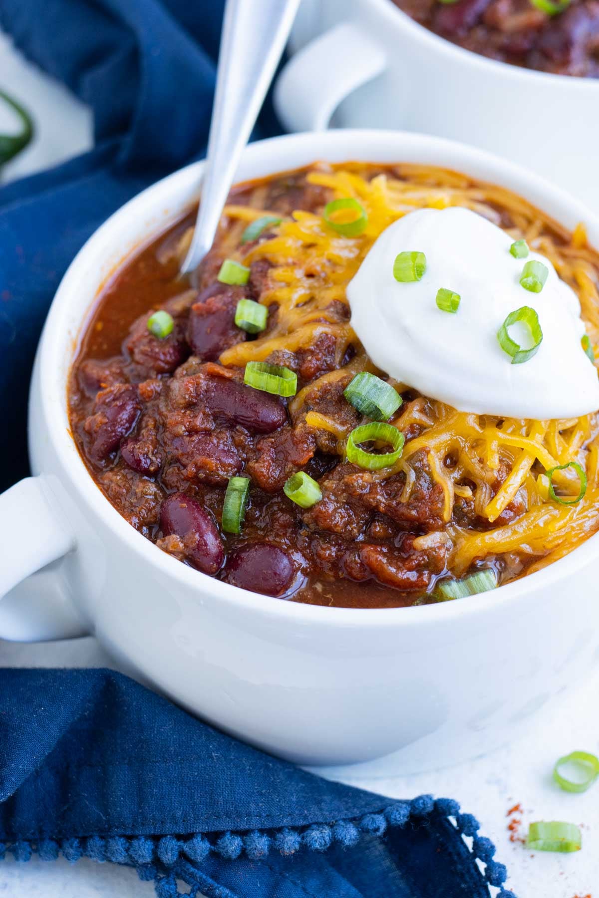 A white bowl of Instant Pot chili topped with cheddar, sour cream, and green onions for game day.
