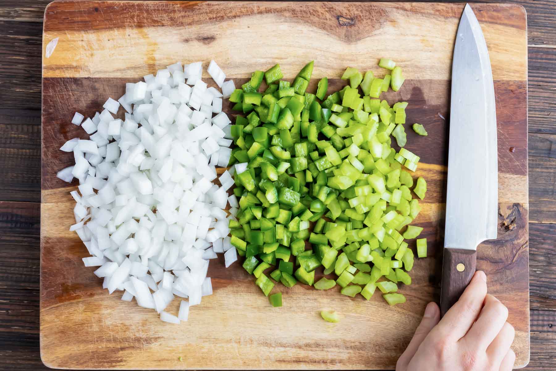 Finely diced onions, green bell pepper, and celery on a wooden cutting board.