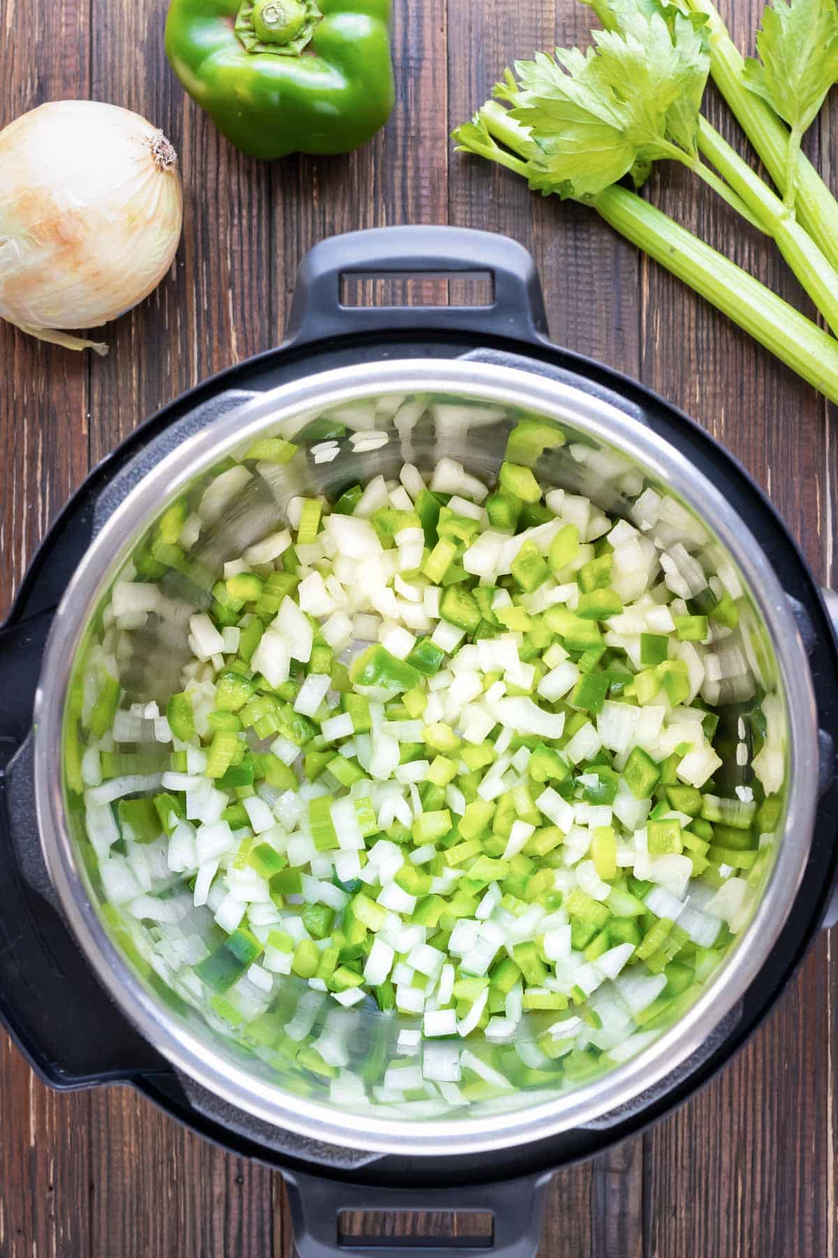 Onions, celery, and bell peppers are added to an Instant Pot.