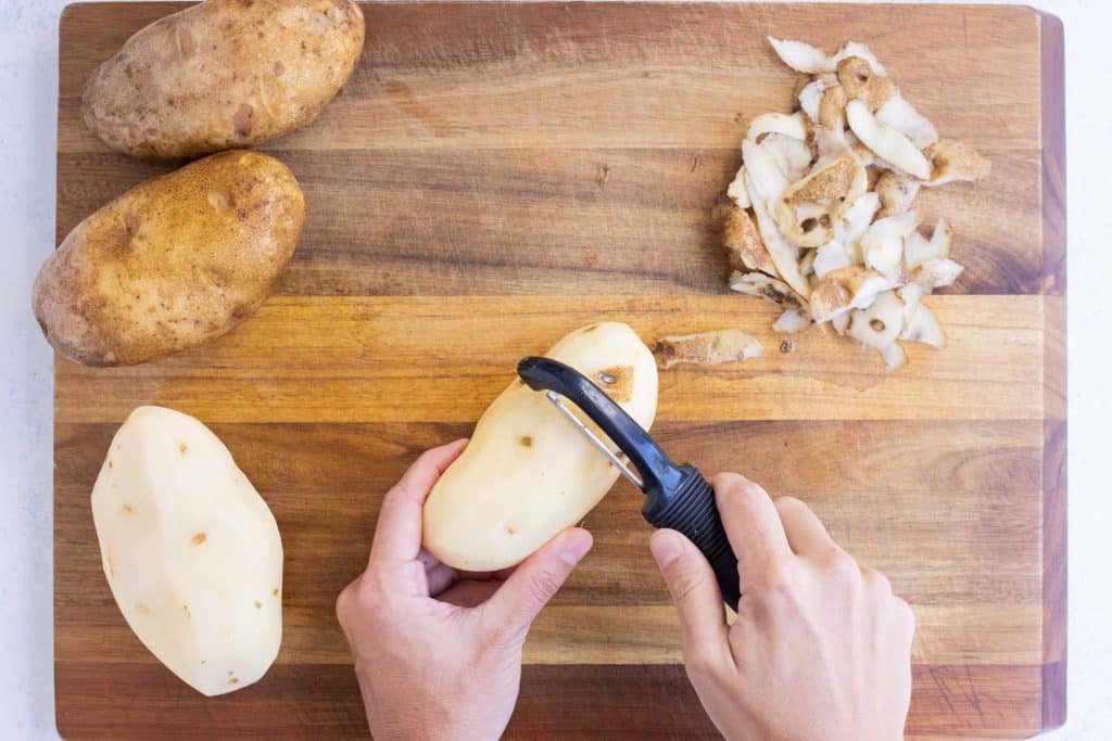 A vegetable peeler removing the skin from a Russet potato.