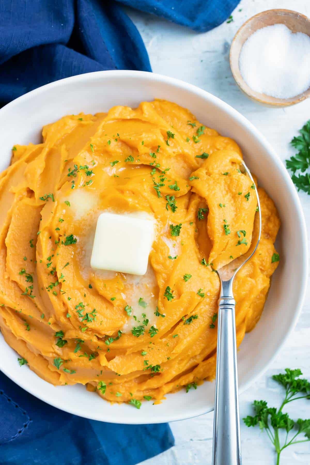 Sweet Mashed Potatoes RECIPE in a white serving dish with a metal spoon garnished with butter.