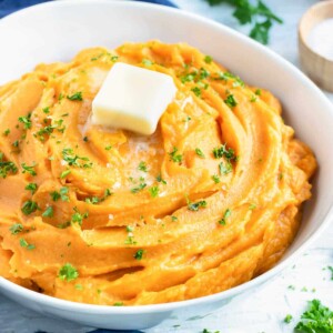 A bowl full of creamy mashed sweet potatoes that are savory with garlic and herbs.
