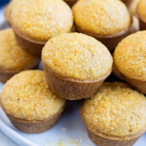 A stack of mini cornbread muffins with honey are served on a plate.