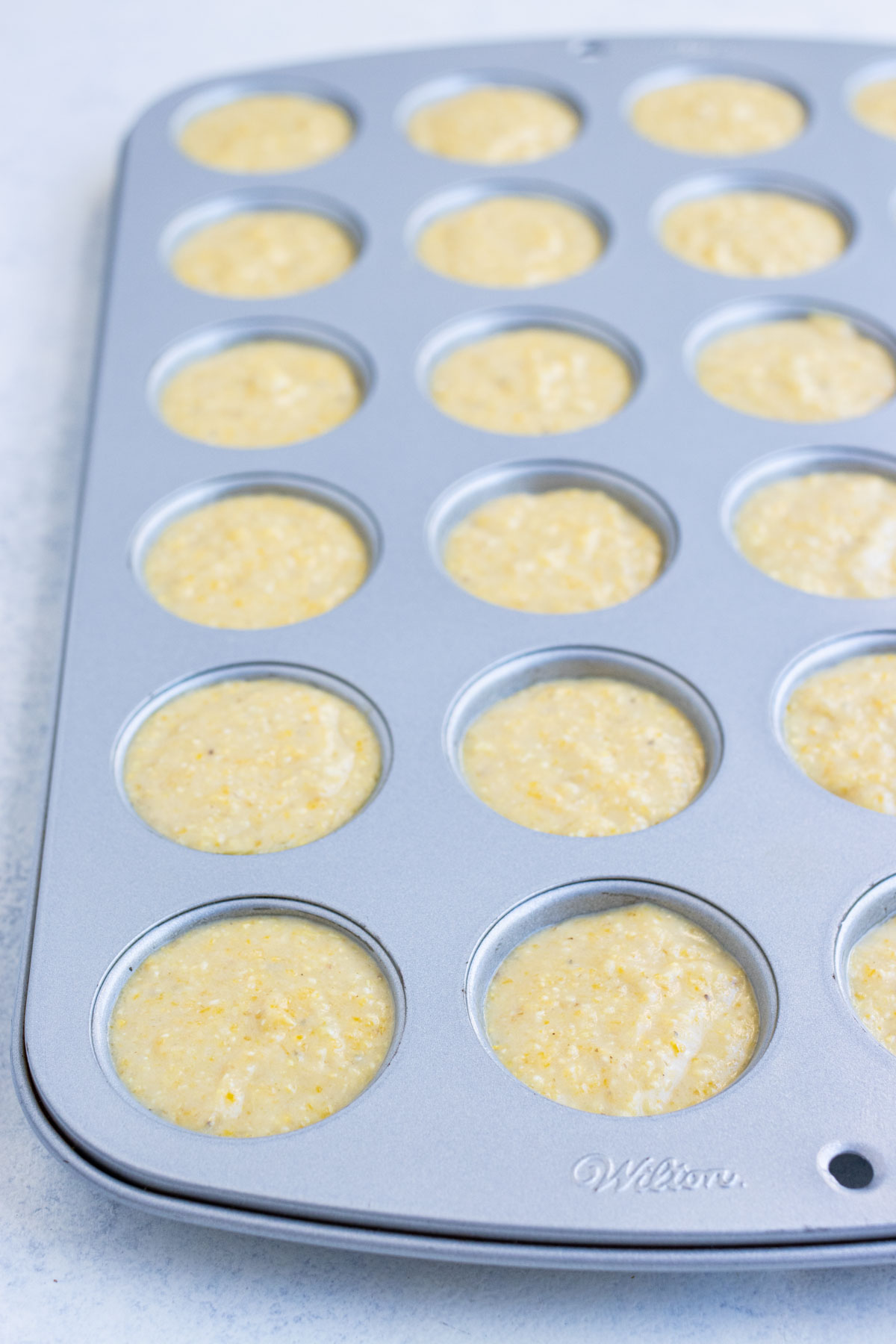 A muffin tin is full of conbread batter.