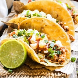 Slow cooker pineapple pulled pork tacos are served with cilantro and a lime.