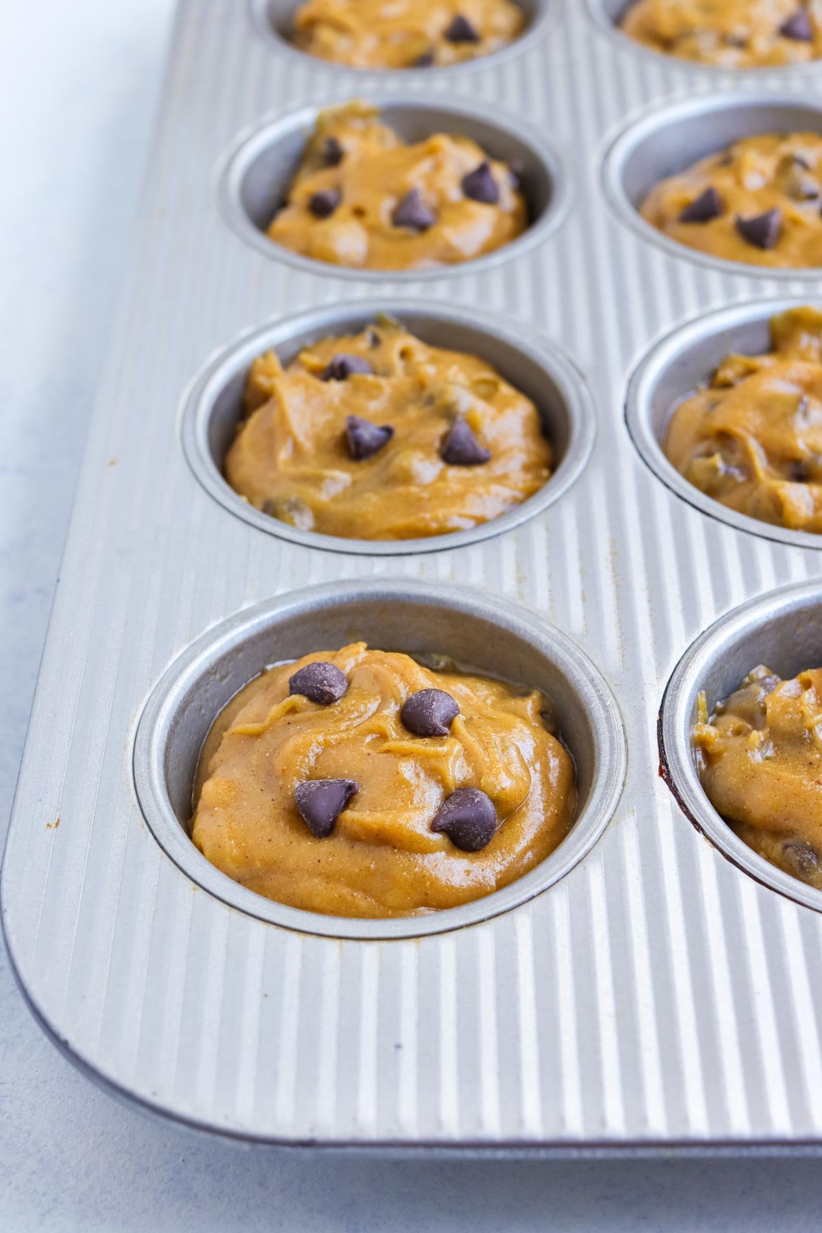 A muffin tin is mostly full of pumpkin muffin batter.