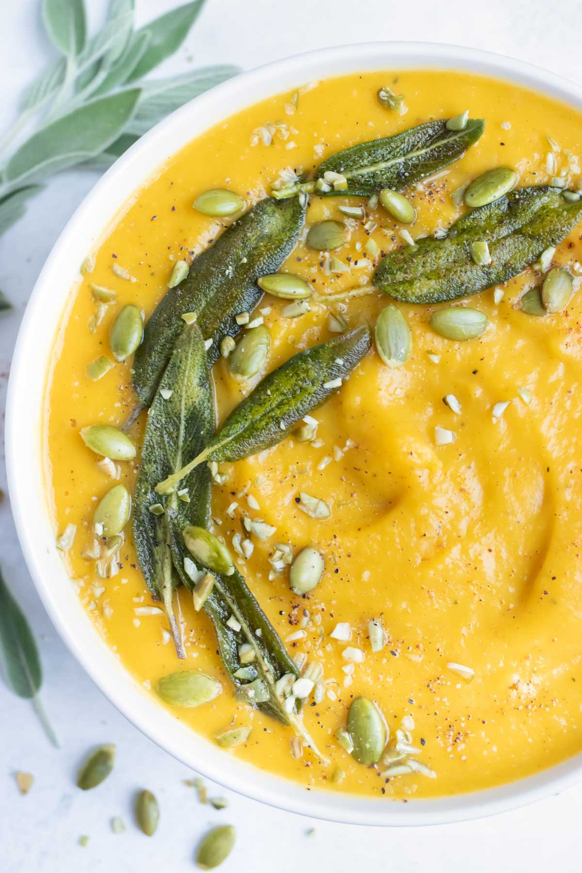 Pumpkin soup is topped with fried sage leaves, roasted pumpkin seeds, and spices.