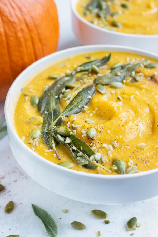 Pumpkin soup is topped with sage leaves and pumpkin seeds for an easy and stunning appetizer.