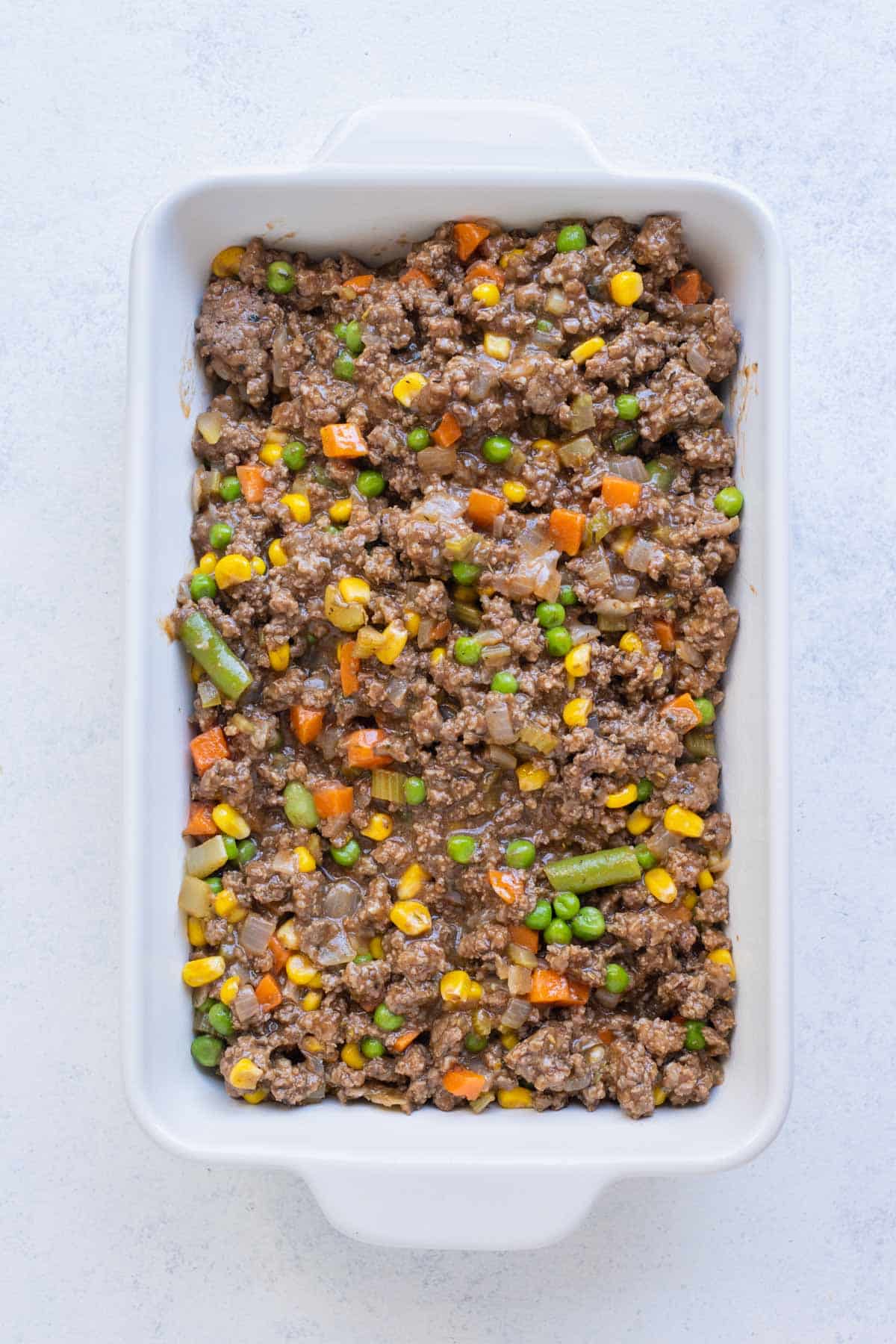 A meat mixture is spread out in a casserole dish.