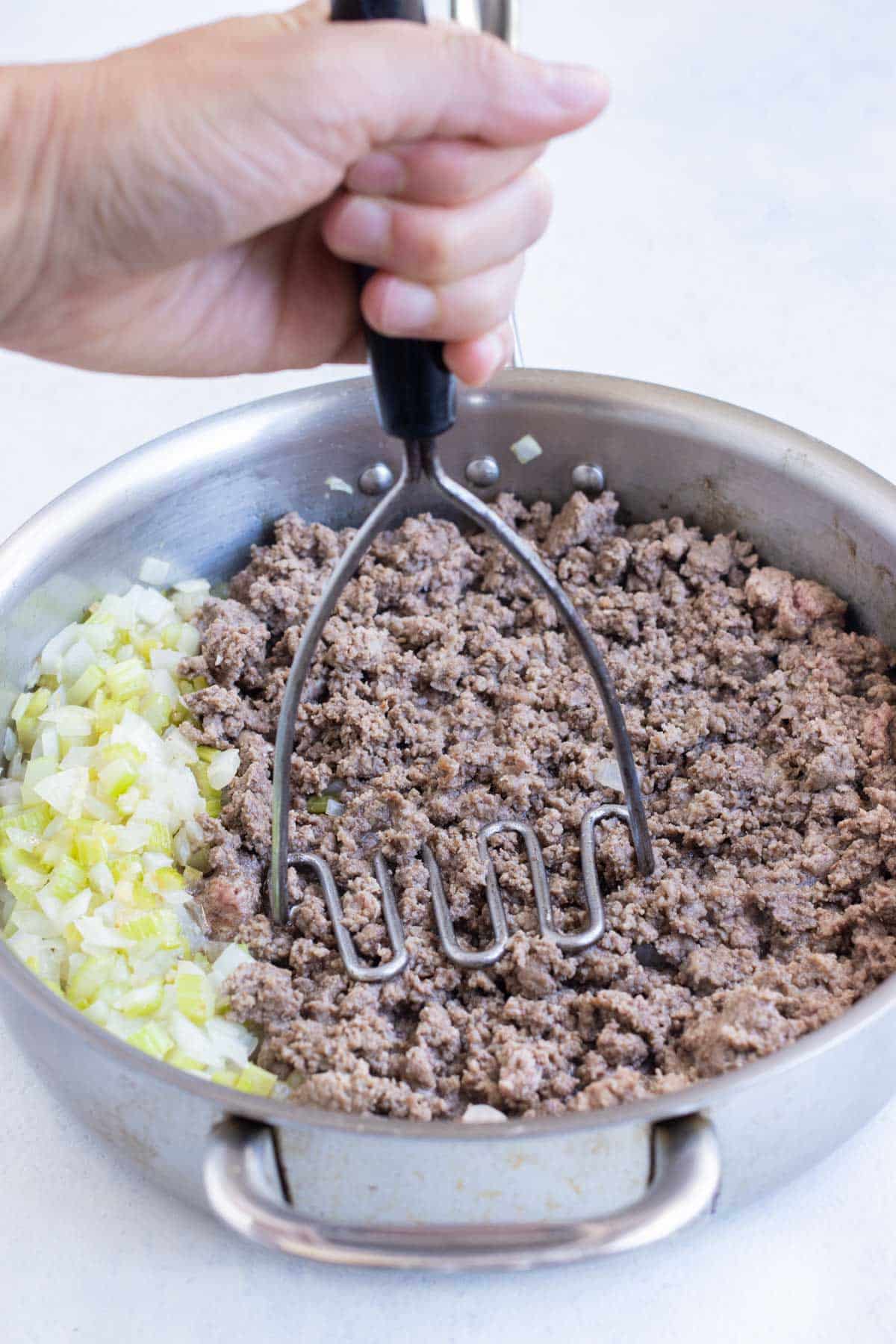 A potato masher crumbles ground beef.