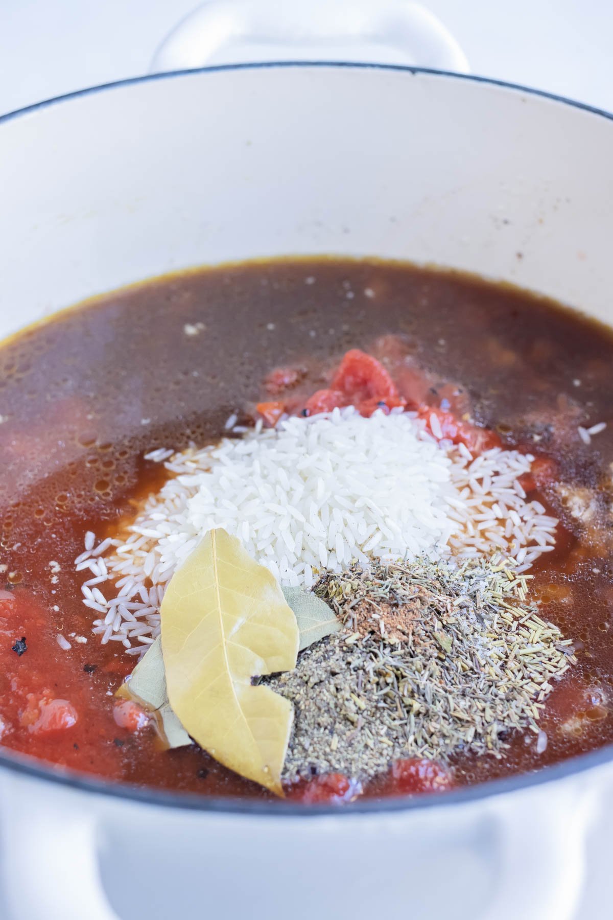 Broth, rice, seasonings, tomatoes and herbs are added to the pot.