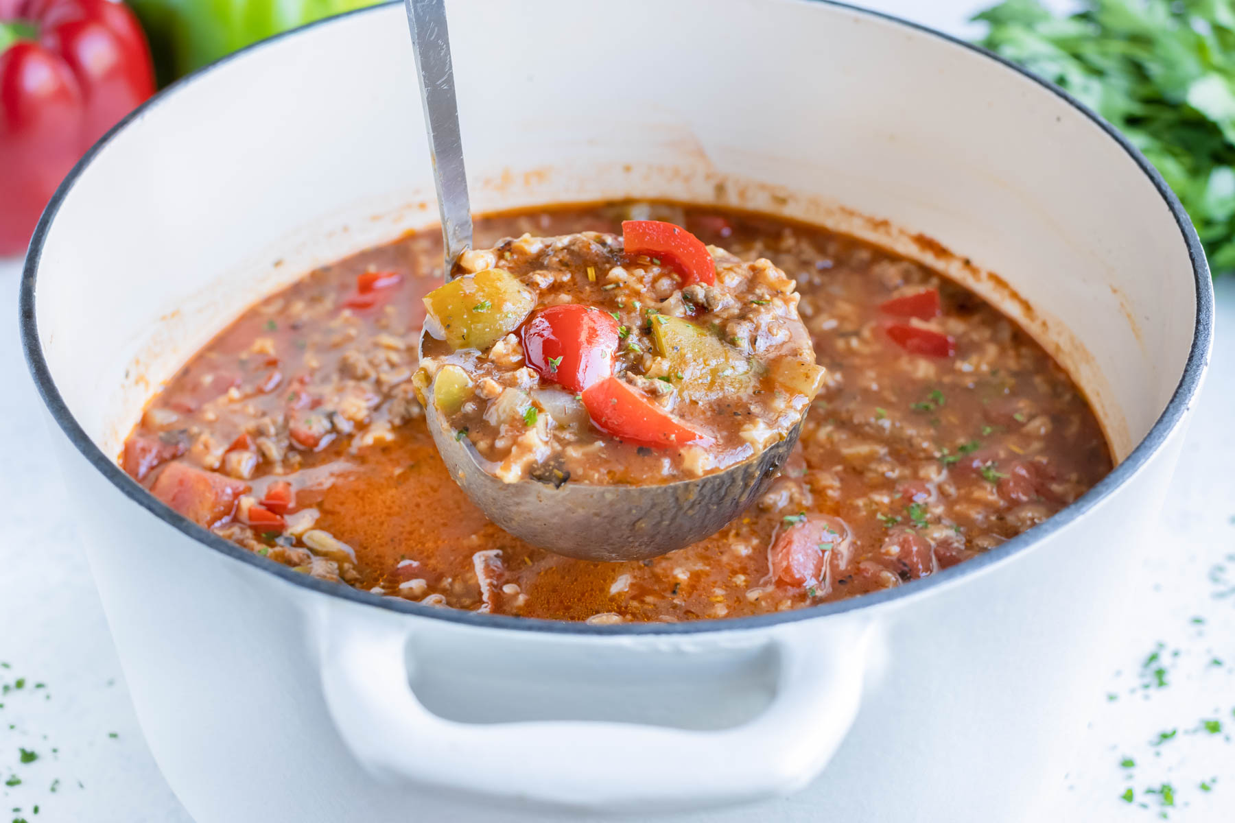 A ladle lifting a scoop of homemade stuffed pepper soup from a white Dutch oven.