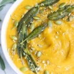 Pumpkin soup is topped with fried sage leaves, roasted pumpkin seeds, and spices.