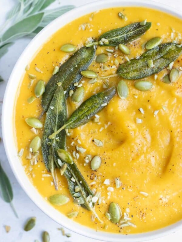 Pumpkin soup is topped with fried sage leaves, roasted pumpkin seeds, and spices.