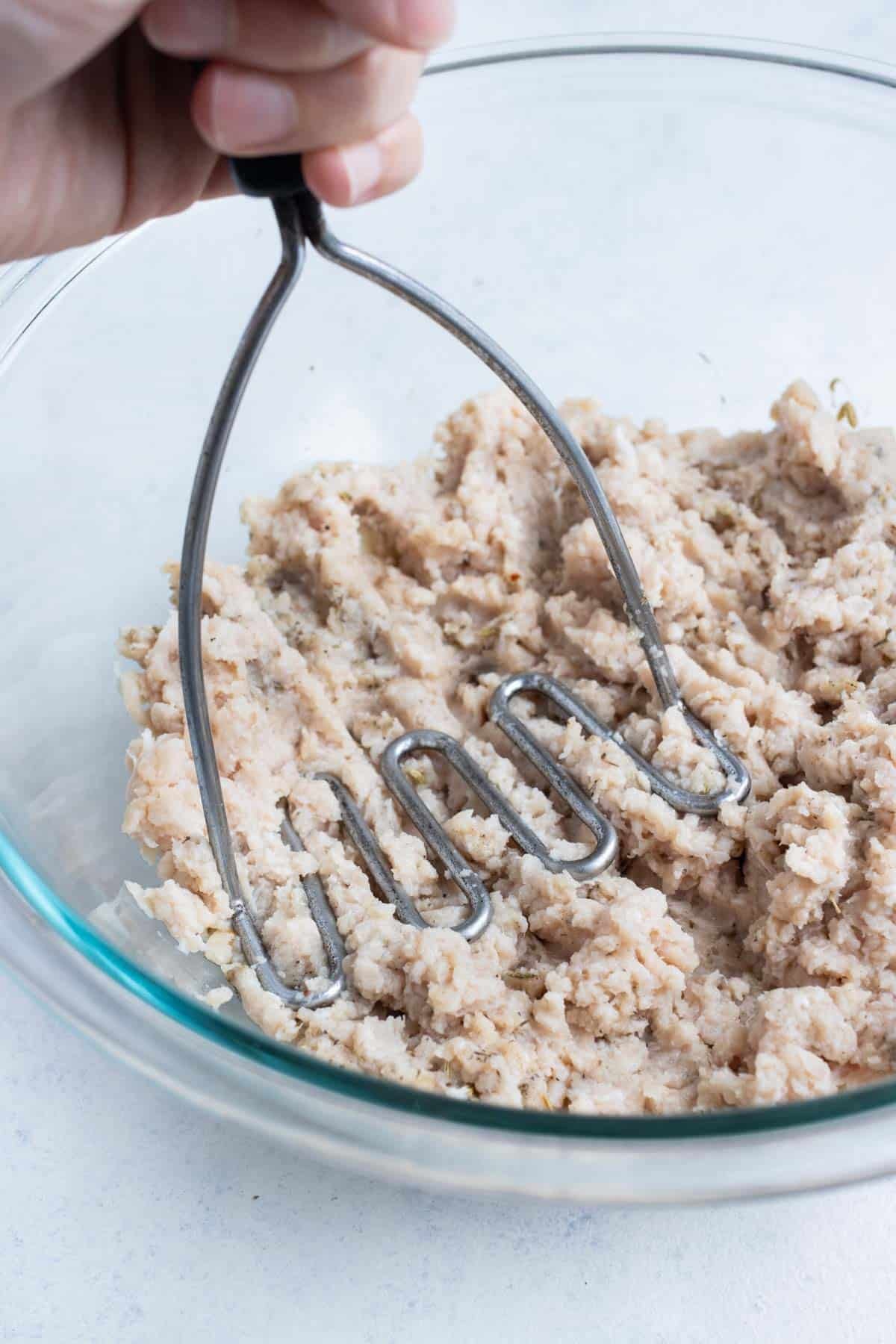 A potato masher mixes the seasoned chicken.