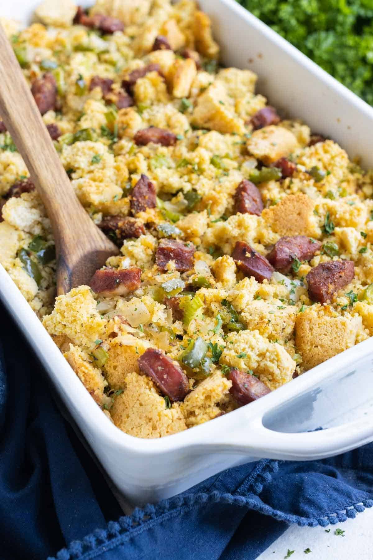 Cajun Cornbread Dressing RECIPE served in a white casserole dish with a wooden spoon.