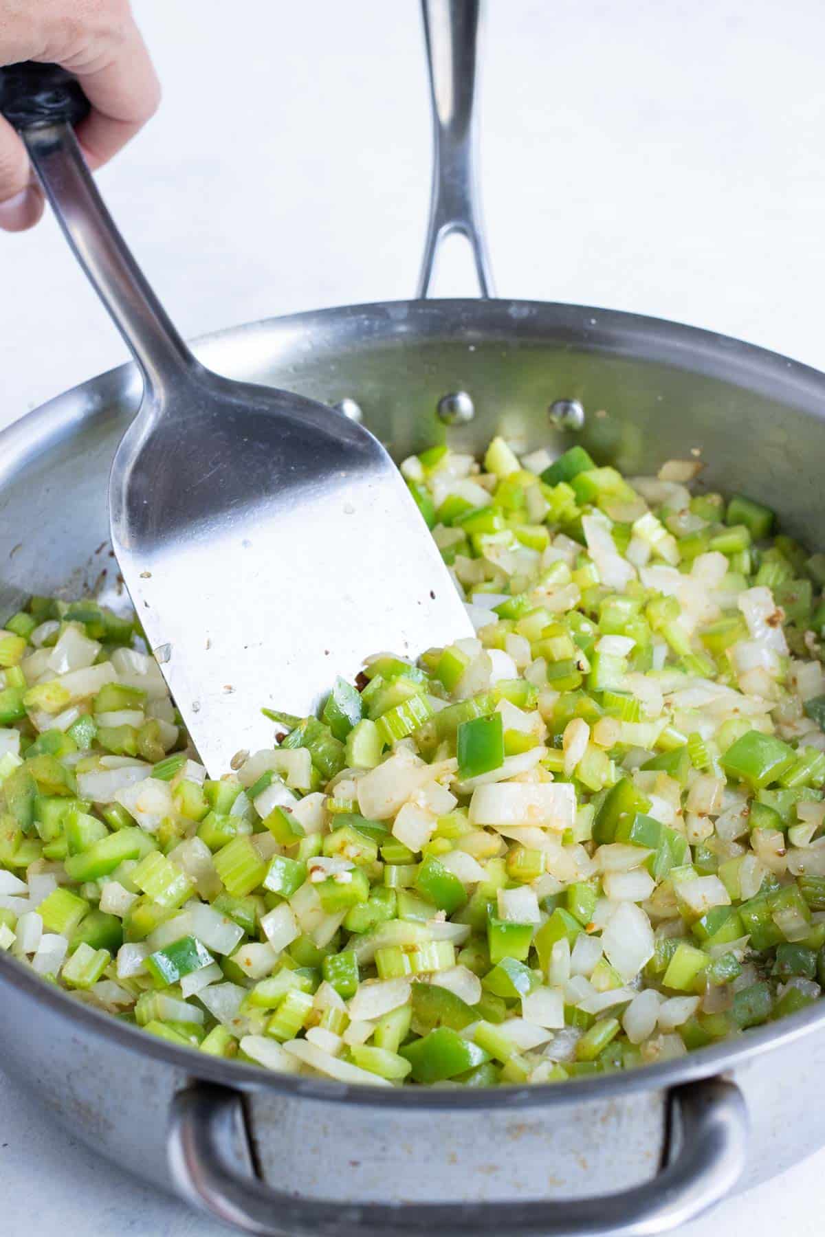 Onions, celery, and bell peppers are sauteed in a pan.