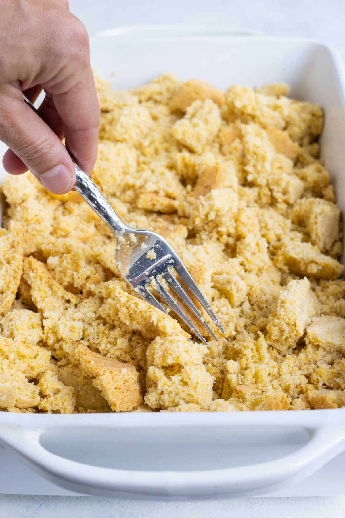 Cornbread is crumbled with a fork.