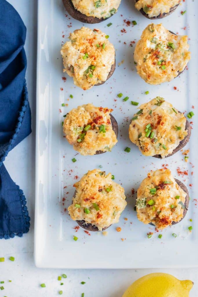 Mushrooms stuffed with a crab filling are lined up on a serving tray.