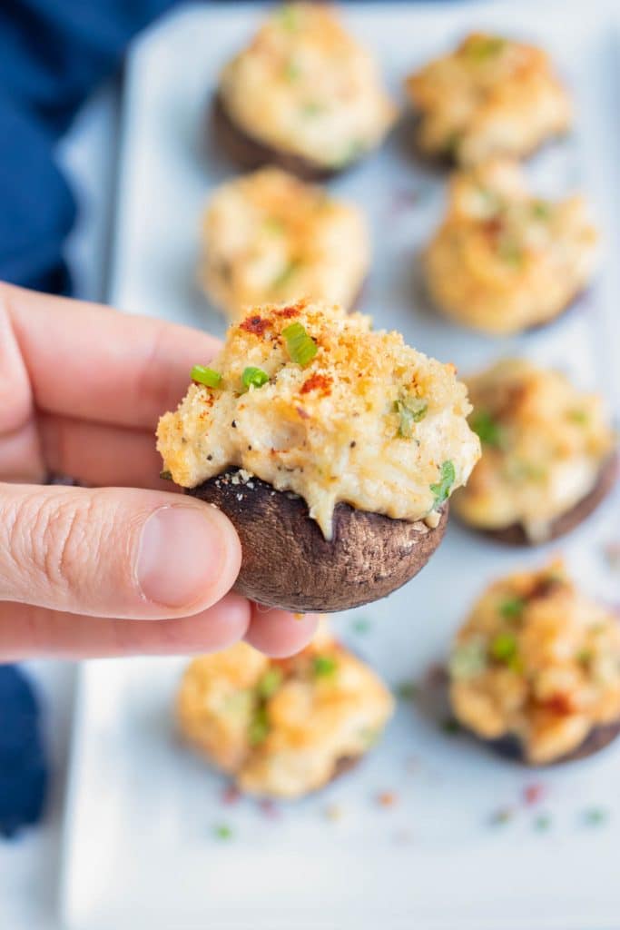 A hand picks up a crab stuffed mushroom from a party tray.