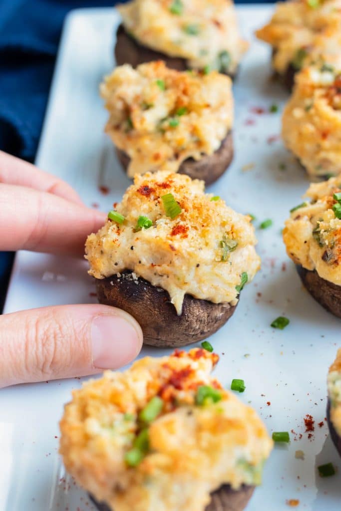 Stuffed mushrooms are grabbed by two fingers to be eaten at a party.